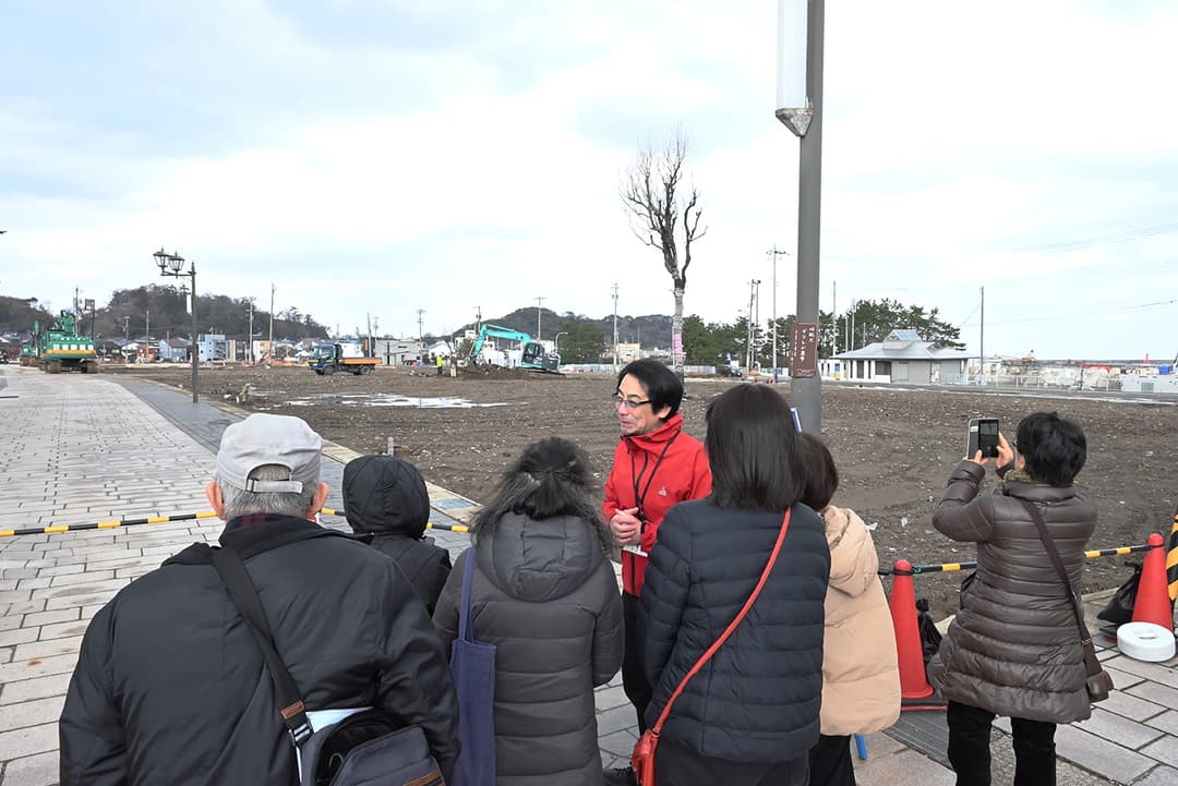 更地になった輪島市河井町本町の朝市通りで、バスツアーの団体客を案内する富水さん(2025年1月撮影)