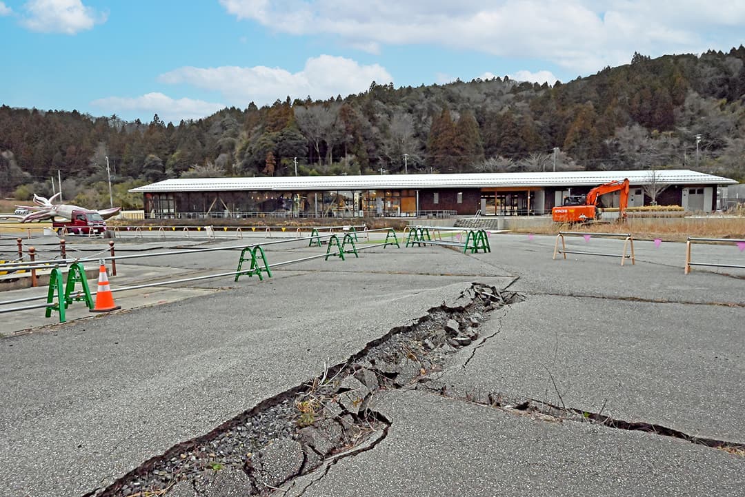 遊覧船乗り場から見た“イカの駅 つくモール”。ここから建物やイカキングを越えて駐車場まで津波が押し寄せ、建物には津波の水位を示す痕跡も残っている(撮影:2026年3月)